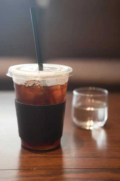 Ice black coffee plastic cup on wooden table in cafe.