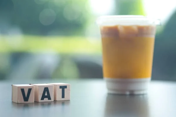 Letter block in word VAT (Abbreviation of Value added tax) with cup of iced coffee background. Financial income have to pay government tax by law. Acronym business concept background