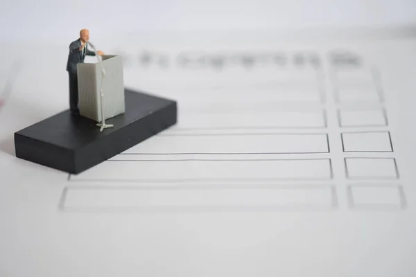Miniature people of a politician speaking with microphone on the podium. Election debates or press conference concept