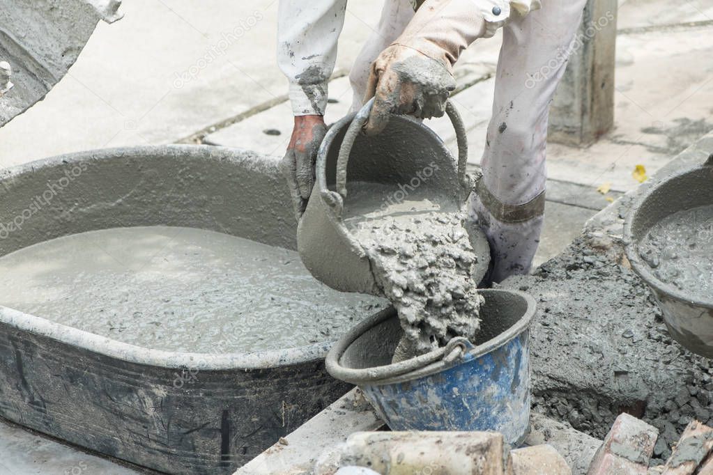 Worker pouring cement mix concrete in bucket at a construction site.