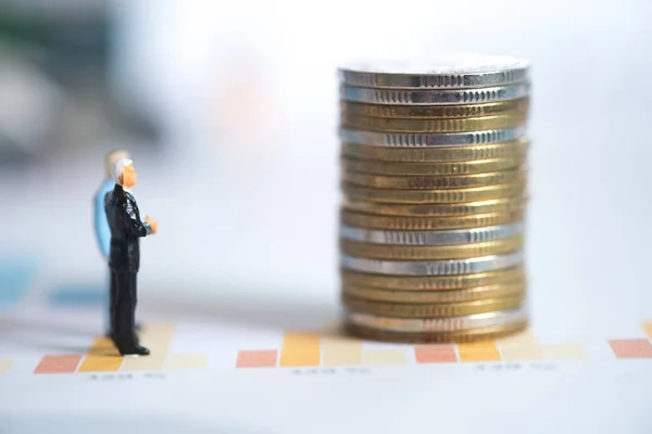Miniature people: Businessman standing on graph with looking and thinking to stack of coins. Concept of Business, Money and Finance.