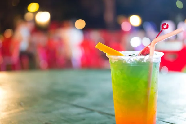 Bright fruit cocktail with orange piece of in a plastic cup on night cafe. Summer fruit drinks
