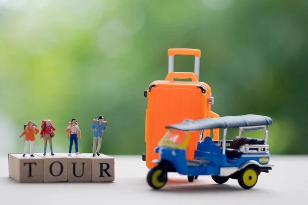 Miniature people : Traveler with backpack standing on wooden word TOUR with tuk-tuk and orange suitcase