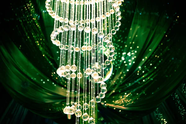 Elegant crystals hanging above wedding reception with green light background