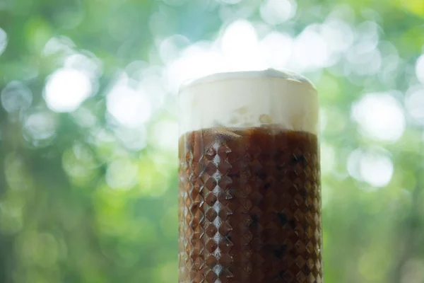 Холодный кофе в стакане с молочной пеной на фоне природы — стоковое фото