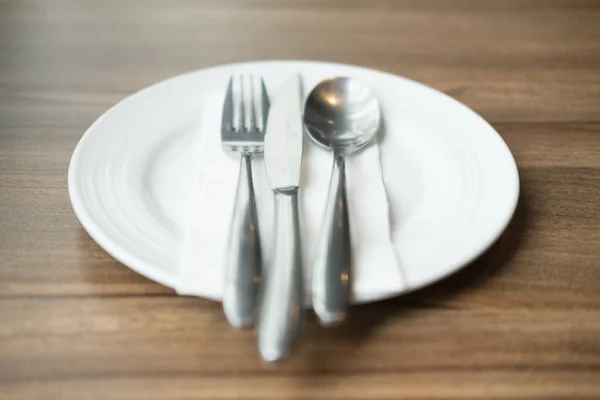 Белая тарелка и столовые приборы на деревянном столе — стоковое фото