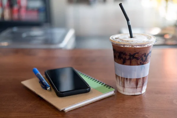 Office desk with cup of iced coffee and phone, pen on brown note — Stock Photo, Image