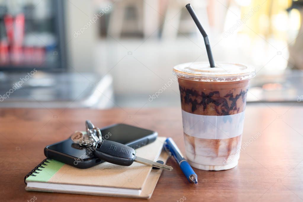 Office desk with cup of iced coffee and phone, car key on notebo