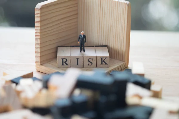 Personas en miniatura: hombre de negocios parado sobre un cubo de madera palabra con riesgo. Concepto de gestión o evaluación del riesgo empresarial —  Fotos de Stock