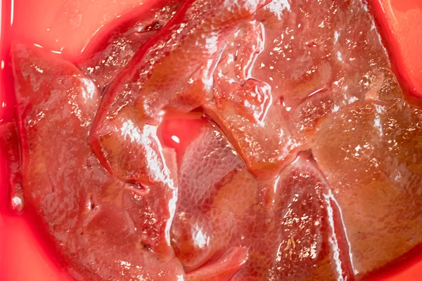 Сырая свежая нарезанная свиная печень на красном лотке — стоковое фото