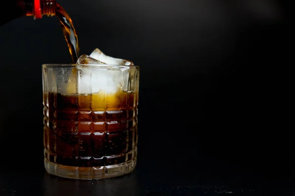 Het gieten van verfrissende Cola van fles in glas met ijsblokjes — Stockfoto