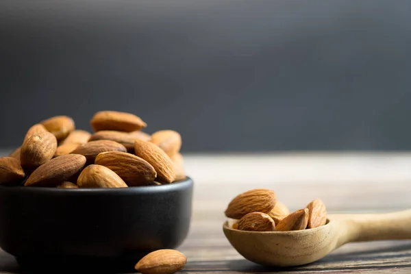 Almonds in black bowl (roasted) on wooden background
