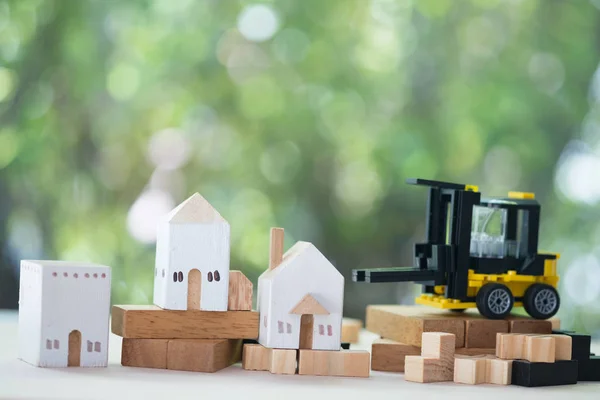 Мініатюрні дерев'яні моделі будинків з мініатюрним жовтим навантажувачем на дерев'яний стіл. Архітектура та будівельна індустрія для розвитку житлового бізнесу. Концепція власності або нерухомості — стокове фото