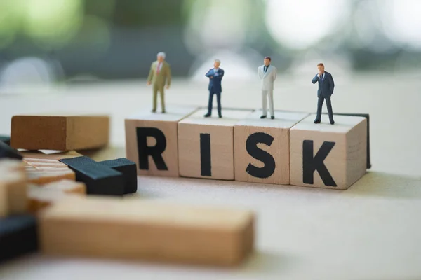 Miniature people group of businessmen stand on cube word with risk. Risk analysis for investment. The concept business risk assessment or management concept