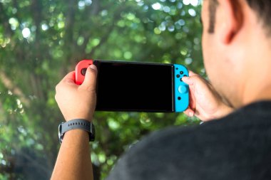 Tayland, Bangkok - 23 Ekim 2019: Nintendo Switch, ev veya taşınabilir oyun konsolu. Genç adam konsolda oyun oynuyor.
