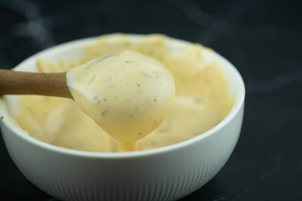 Используйте деревянную ложку соус для салата Цезаря из белой миски
