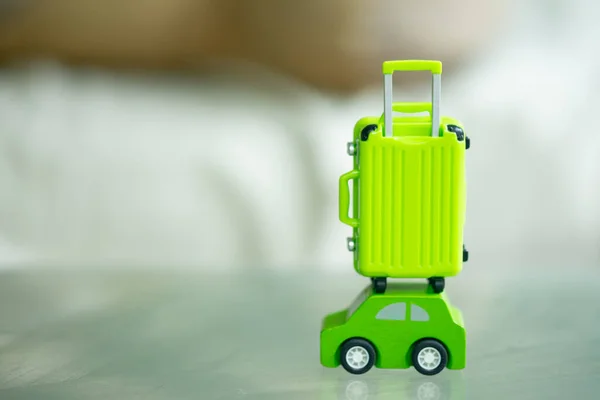 Miniature green travel suitcase on wooden green car. Concept of travel