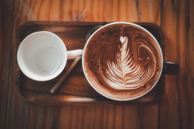 Ahşap masanın üstünde köpüklü sanat eserleriyle nefis sıcak çikolata.