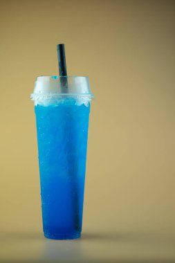Uzun plastik bardakta buzlu mavi limonlu soda ve siyah pipet.
