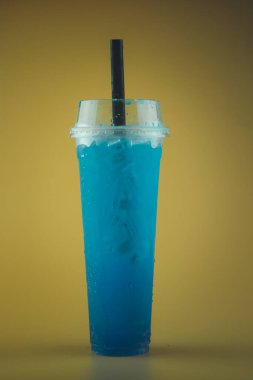 Uzun plastik bardakta buzlu mavi limonlu soda ve siyah pipet.