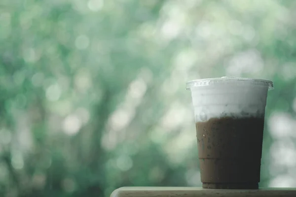 Iced Mocha coffee in takeaway glass and milk foam with nature background. Show Layer milk foam and coffee