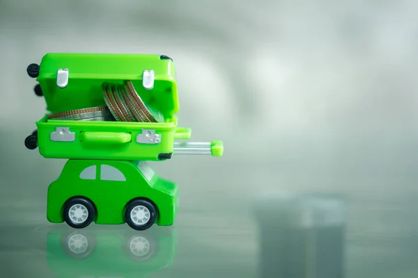 Yeşil arabanın üzerinde minyatür yeşil bavul dolusu para. Seyahat için para biriktirme kavramı.