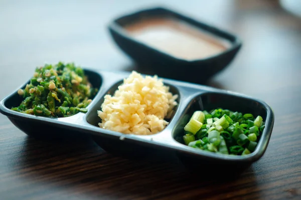 Set of slice vegetable, garlic, chill and chives on black tray for topping sauce in shabu style