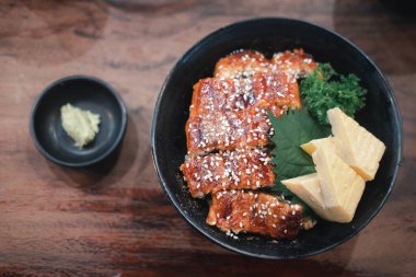 Ahşap masada siyah kasede ızgara yılan balığı.