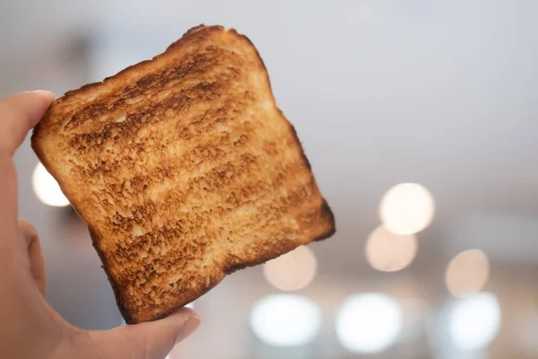 Man holding up a toast was burnt during toasting.  Burnt toast at breakfast.