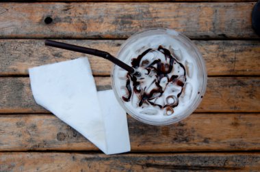 Üstünde çikolata sosu ve kağıt mendil olan taze buzlu süt dolu plastik bardağın en üst görüntüsü..