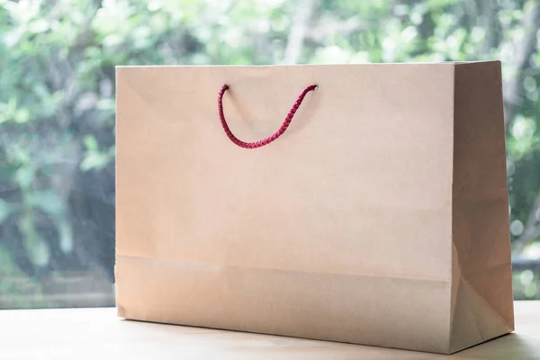 Blank brown paper bag with red handle on wood table
