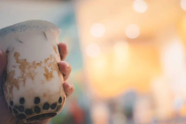 Man is holding and showing a plastic cup of brown sugar flavor tapioca pearl bubble milk tea