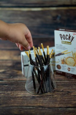 Samut Prakan, Tayland - 19 Ağustos 2020: El yapımı küçük çocuk çikolata soslu bisküviler bardaktan yeni aromalı Glico Pocky Wholesome bisküvisi alıyor