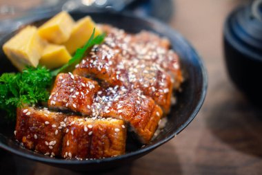 Ahşap masada siyah kasede ızgara yılan balığı.