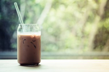 Bardakta buzlu kahve ve ahşap masadaki camdan yapılmış saman.