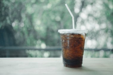 Plastik bardakta meşrubat, ahşap masada yeşil arka planda.