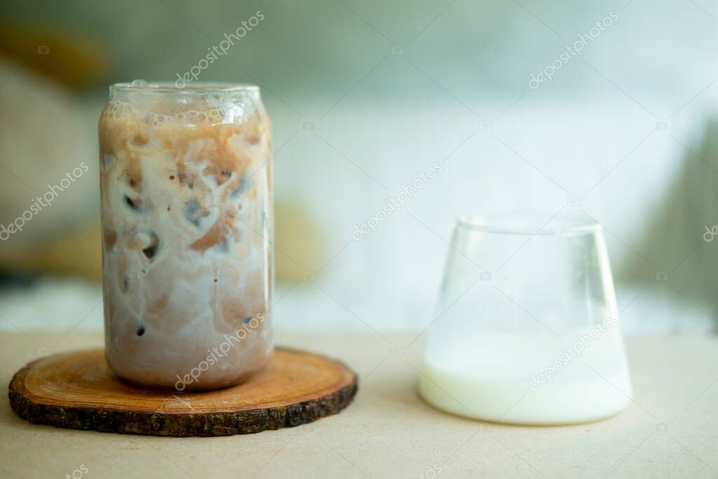Iced coffee on a wood table with fresh milk being poured into it showing the refreshing drink