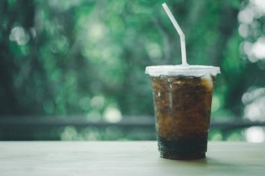 Plastik bardakta meşrubat, ahşap masada yeşil arka planda.