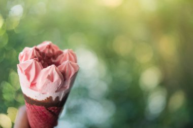 El ele tutuşup pembe waffle külahı ile doğanın bulanık arka planında çilekli dondurmanın görüntüsünü kapat.