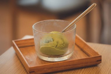 Ahşap tepside servis edilen cam kasede yeşil çay, kibritli dondurma.