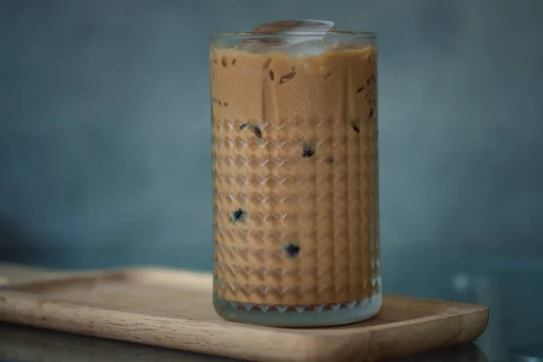 Iced coffee mixing with milk and chocolate in glass on wood tray