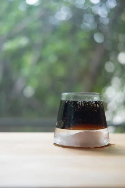 Glass of soft drink with ice on wood table and nature background