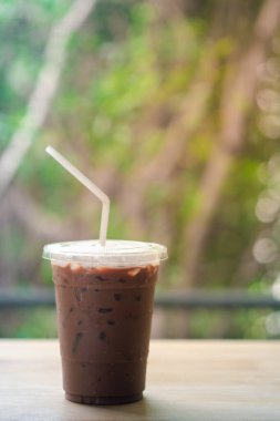 Buzlu kahve Mocha tek kullanımlık plastik bardakta ve ahşap masada beyaz saman var.