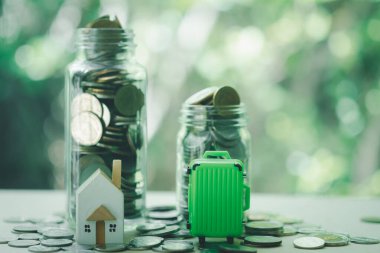 Minyatür ev ve cam şişenin içinde madeni para bulunan yeşil bavul. Ev ve seyahat konsepti için para biriktiriyorum