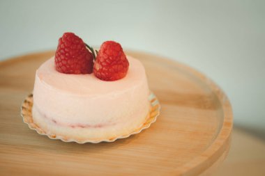 Yuvarlak bir ahşap tezgahta, üzerinde pembe krema gülü ve böğürtlen olan pembe kremalı pasta.