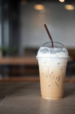 Kahve dükkanındaki ahşap masada plastik bardakta buzlu kapuçino ve süt köpüğü.