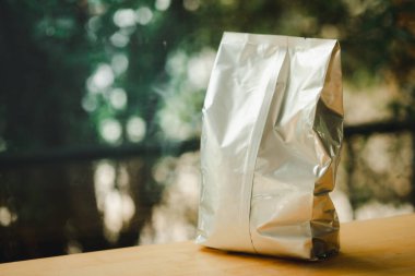 Ahşap sehpanın üzerinde gümüş renkli parlak folyolu kahve poşeti. Perakende satış ve reklam konsepti.