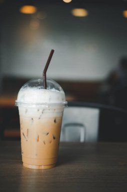 Kahve dükkanındaki ahşap masada plastik bardakta buzlu kapuçino ve süt köpüğü.