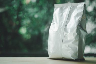 Ahşap sehpanın üzerinde gümüş renkli parlak folyolu kahve poşeti. Perakende satış ve reklam konsepti.