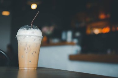 Kahve dükkanındaki ahşap masada plastik bardakta buzlu kapuçino ve süt köpüğü.